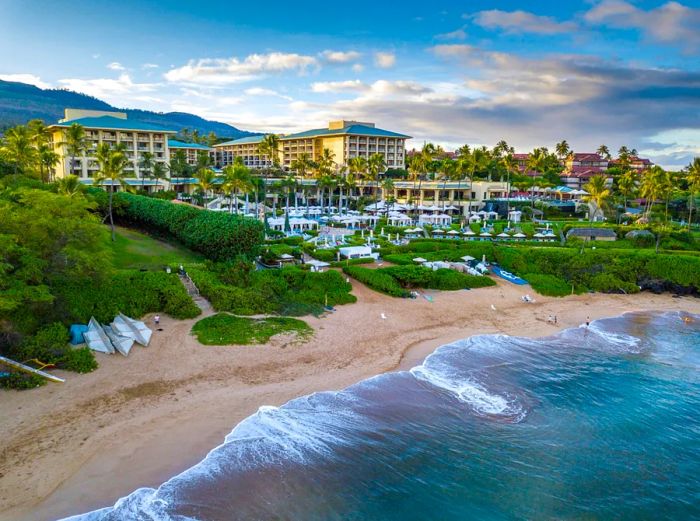 A distant view from the ocean of the Four Seasons Resort Maui at Wailea, featuring a nearly deserted beach in the foreground.