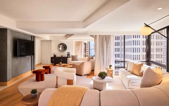 A hotel room featuring neutral-toned furnishings, including a spacious curved sofa and large windows