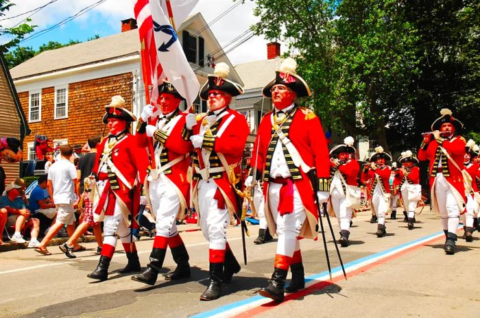 Adults clad in British red coats from the American Revolution participate in a parade.