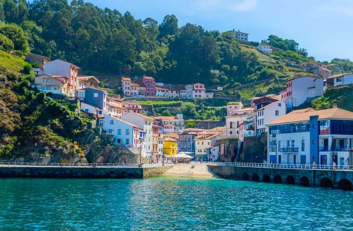 A village perched on hillsides, viewed from the water, surrounded by lush green trees