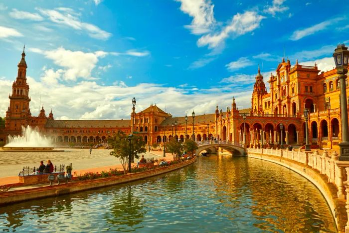 Waterway connecting the plaza with a fountain (to the left) and historic buildings in Seville
