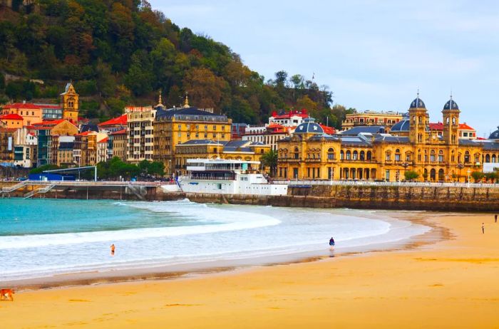 A few people strolling along a wide, flat beach adjacent to historic buildings