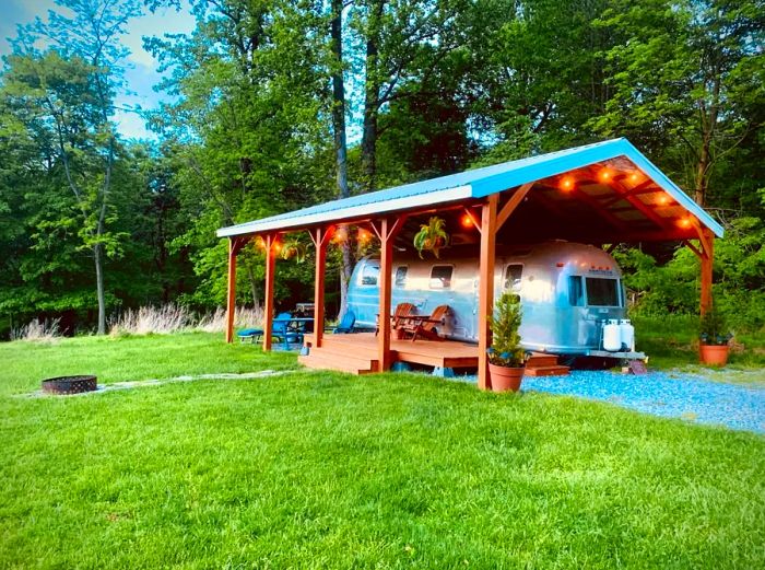 Airstream trailer beneath a roof with open sides, surrounded by lush grass and trees