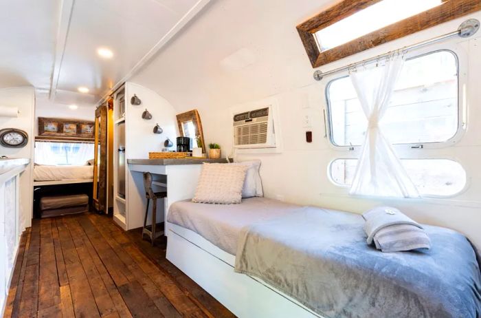 The bright interior of an Airstream trailer showcasing reclaimed dark wood floors and a cozy bed