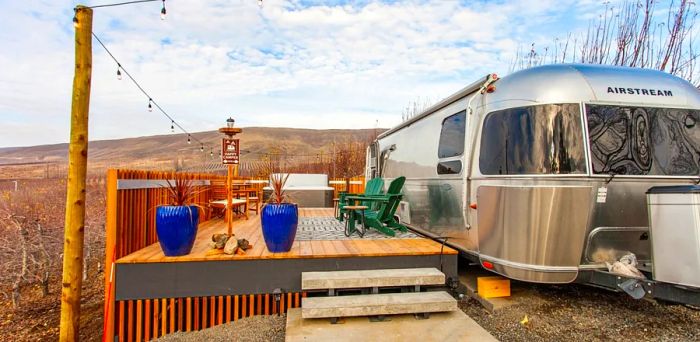 Airstream trailer adjacent to a wooden patio, with a tan mountain valley in the backdrop