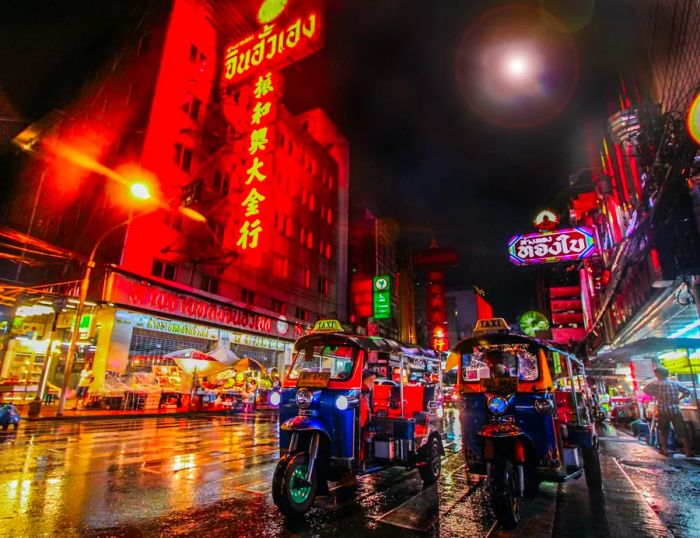 A vibrant scene in Bangkok's Chinatown at night, with tuk-tuks passing by neon-lit streets.
