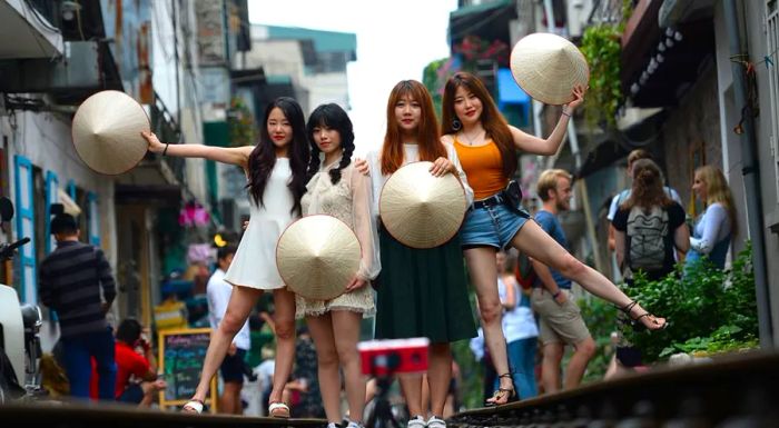 A group of tourists strike a pose with traditional Vietnamese conical hats on the train tracks.