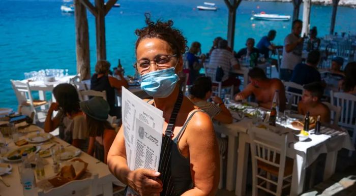 Waitress Vasiliki Besiou wears a face mask as she serves customers at Takis Taverna, located in the charming coastal village of Limeni.