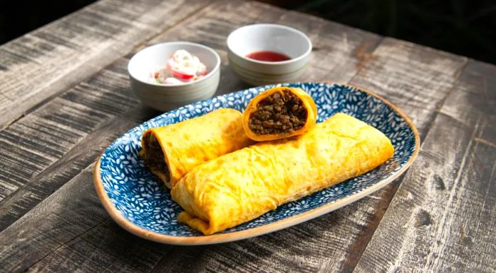 Beef murtabak from Singapore is a savory egg crepe stuffed with seasoned ground beef, typically served with fresh lime, chili sauce, and cooling raita.