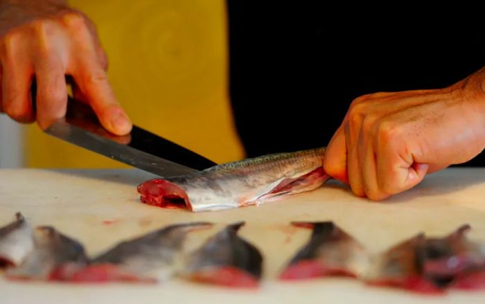 A Japanese chef skillfully slices sea bream during a sushi demonstration.