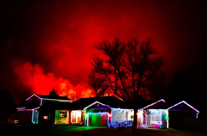 Christmas lights twinkle on a house while the Marshall Fire burns in the background on December 30, 2021, in Louisville, Colorado.