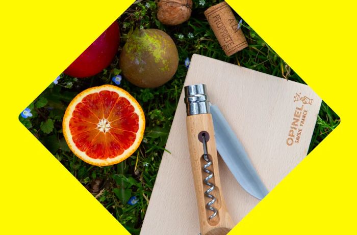 An overhead shot of a knife and corkscrew on a cutting board with some fruit and a wine cork.