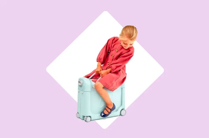 A little girl in a pink dress rides a suitcase designed for kids, making travel a fun adventure.