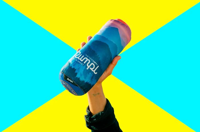 A hand holding a cylindrical carrying case, about the size of a water bottle, with a blanket inside