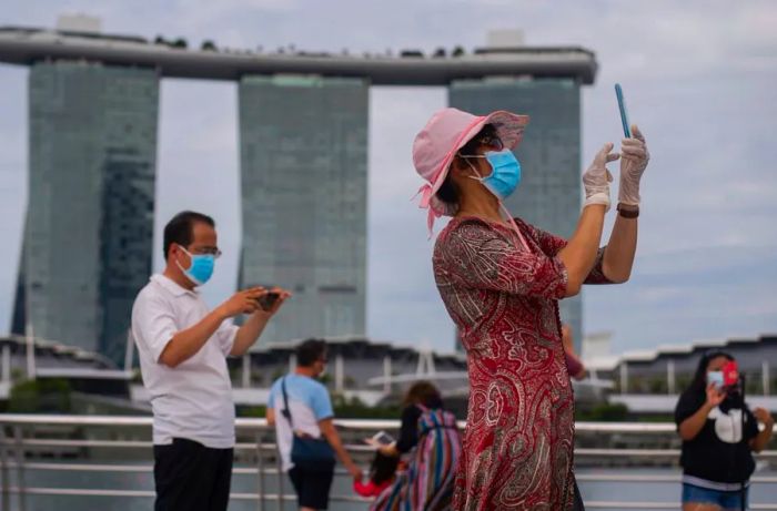 On August 1, 2021, a woman wearing a mask and gloves takes photos at Marina Bay in Singapore.