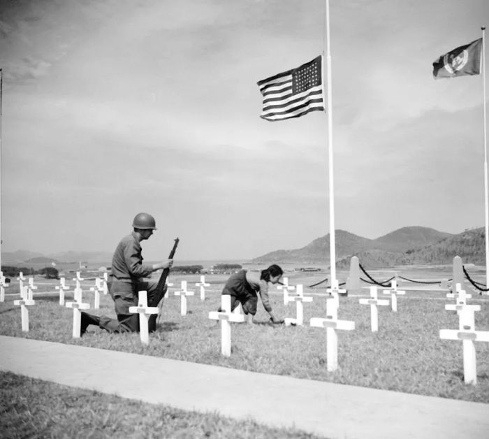 In 1951, an American corporal watches as a young 9-year-old Korean girl lays a bouquet of white roses on the grave of one of his fallen comrades at a UN memorial near Busan, South Korea.