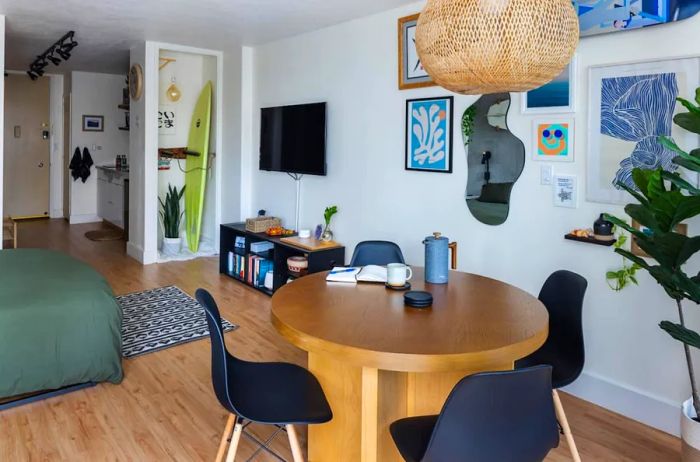 A modern studio apartment featuring a circular table with black chairs, potted plants, and artwork on the wall, including a freeform mirror.