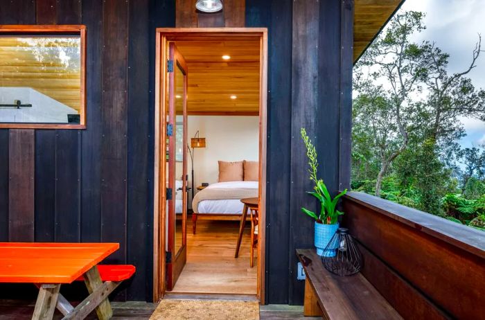 A peek inside a tiny home through the open door, with an orange picnic table on the patio and black wooden walls.