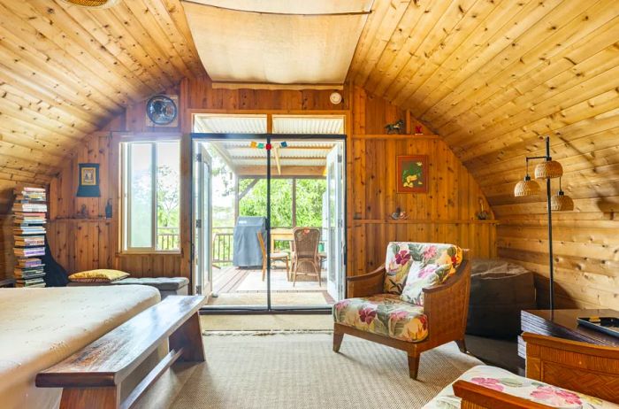 A cedar-lined, semi-circular home featuring floral-patterned chairs, a cozy bed, and sliding glass doors that open to a private patio.