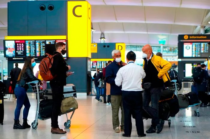 At Heathrow Airport's Terminal 2 in London on December 21, travelers wearing face masks wait at check-in counters as several countries worldwide imposed travel bans on those arriving from the UK.