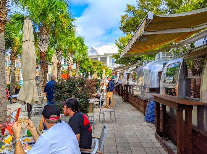 Diners enjoying meals outdoors beside Airstream food trucks, all under swaying palm trees in downtown Pensacola.