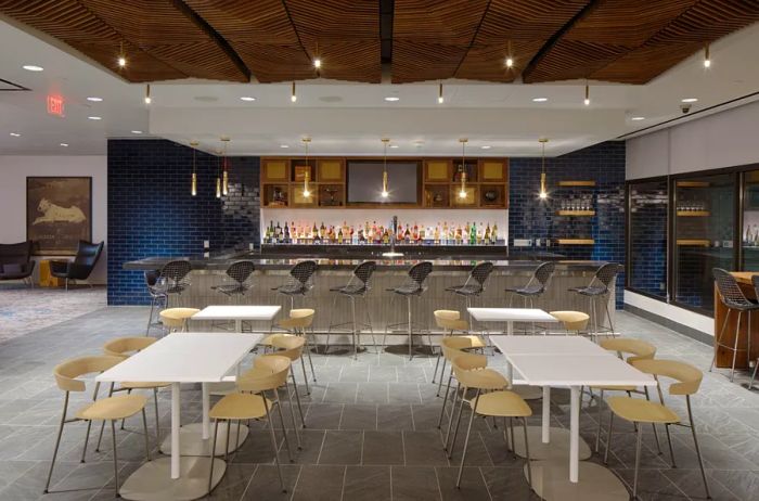 The American Express Centurion Lounge bar in Phoenix, featuring white tables and beige chairs in the foreground.