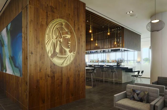 A row of empty bar stools inside the LGA Centurion Lounge, set against a wood wall featuring the AmEx logo – a profile of a helmeted man’s head.