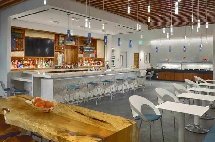 American Express Centurion Lounge Bar at IAH Airport, featuring hanging lights and empty chairs, with a mostly white color scheme accented by wood.