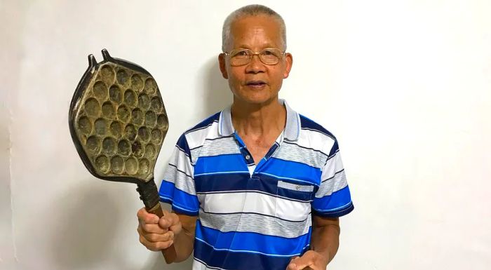 Lee Sui Yuen, a retired egg waffle vendor, proudly holds one of his vintage waffle irons from decades ago.