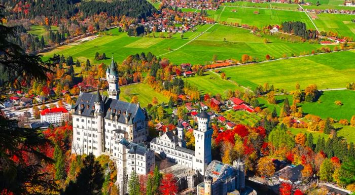 An overhead shot of the iconic Neuschwanstein Castle nestled in the heart of Bavaria, surrounded by the vibrant hues of autumn.