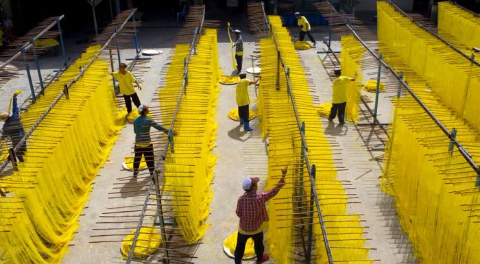 Workers are seen removing longevity noodles from drying racks at a factory in Thailand.