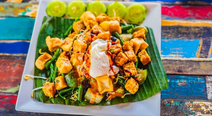 A traditional gado gado features a mix of chopped vegetables, a hard-boiled egg, and occasionally slices of tofu or tempeh, all drizzled with a savory roasted peanut sauce.