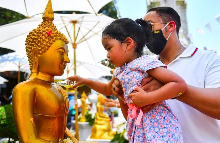 A girl pours water over a Buddha statue as part of the Songkran holiday, performing the Song Nam Phra ritual.