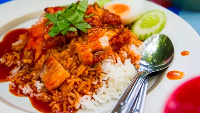 Kao moo dang is a beloved comfort food that can be found everywhere. This dish features a serving of rice topped with thinly sliced Thai barbecued pork, a few slices of Thai sausage, and half of a hard-boiled egg.