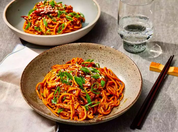 Two plates of slow cooker honey garlic chicken noodles paired with a glass of sparkling water