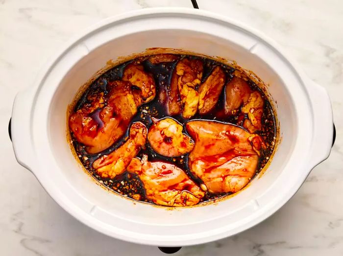 Seasonings and chicken arranged in a slow cooker