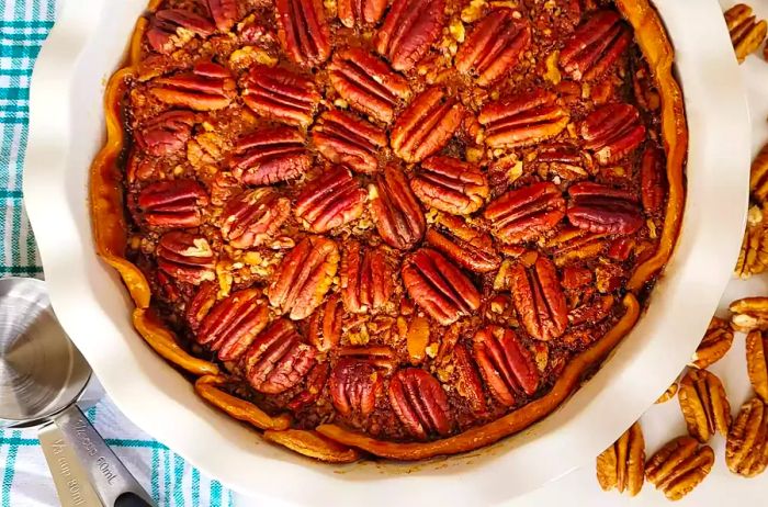 A top-down view of a traditional southern pecan pie in a white pie dish, set on a blue and white checkered linen.