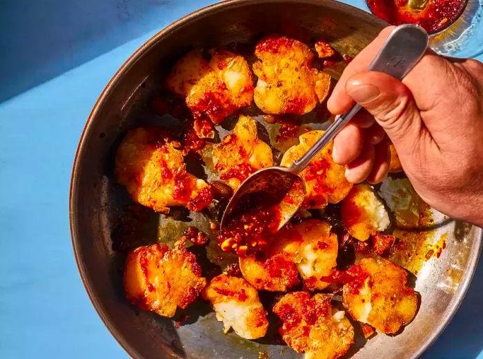 A skillet filled with crispy smashed baby potatoes, drizzled with chili crisp on top.