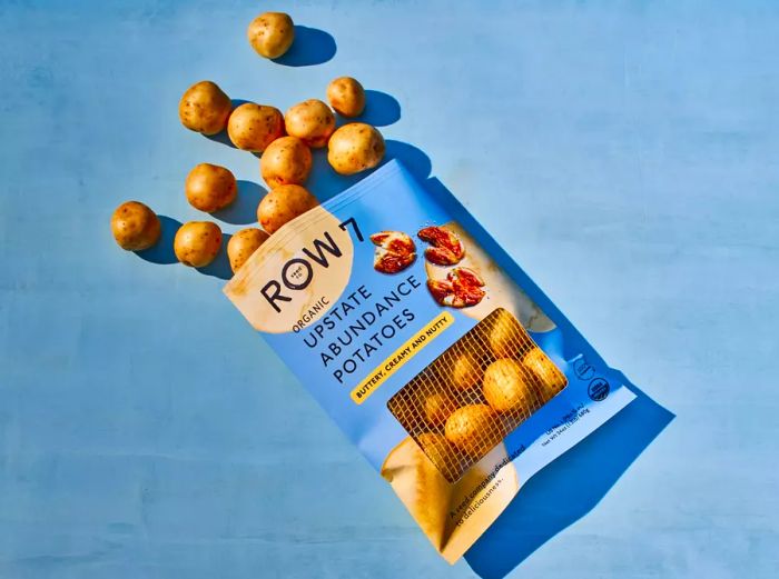 A bag of Row 7 Organic Upstate Abundance Potatoes with golf ball-sized white potatoes spilling out of a blue package.