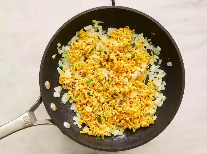 A skillet with sautéed onions and noodles added to the mix.