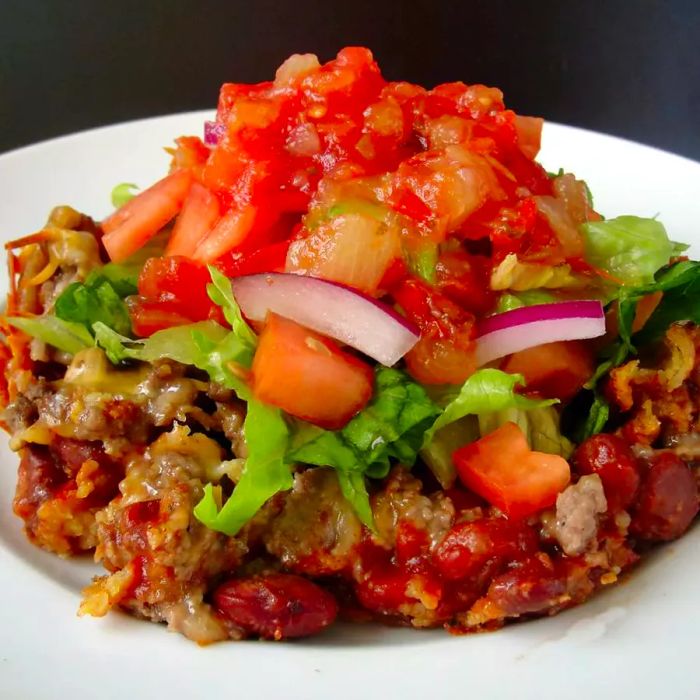 A close-up shot of Taco Casserole with lettuce, red onions, and salsa served on a white plate.