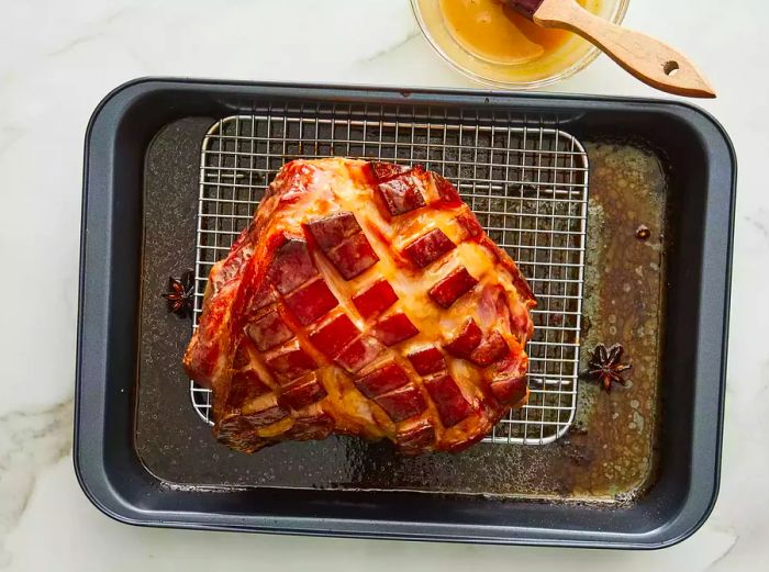 Top-down view of a roast on a wire rack, with glaze being applied over the surface.