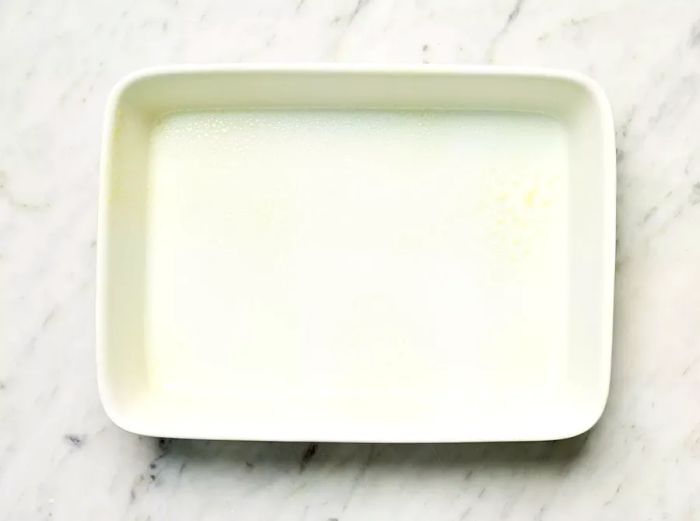 Greased white casserole dish placed on a marble countertop