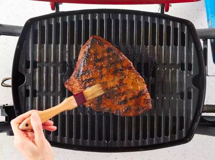 Brushing sauce onto a Santa Maria Grilled Tri-Tip Beef as it cooks on the grill