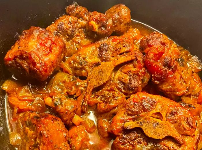 A close-up view of braised oxtails simmering in red wine sauce in a pot.