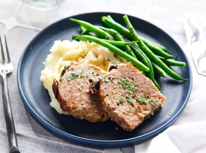 Two hearty slices of meatloaf served on a bed of creamy mashed potatoes with a side of fresh green beans.