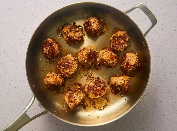 The meatballs being browned in the skillet.