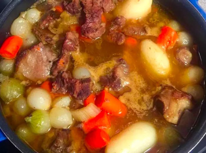 A close-up view of oxtail soup with carrots and onions simmering in a pot.