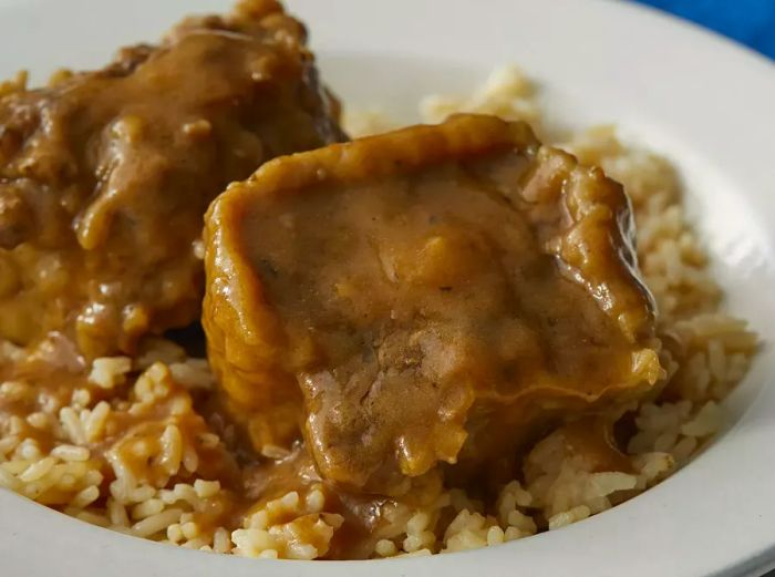 A high-angle view of a plate of oxtails smothered in gravy, served over rice.