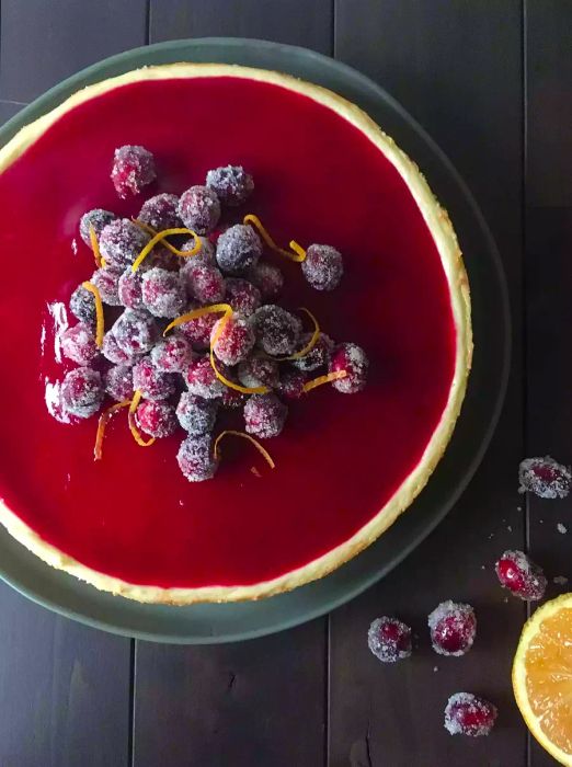 cheesecake topped with a vibrant cranberry glaze, sugared cranberries, and delicate curls of lemon zest